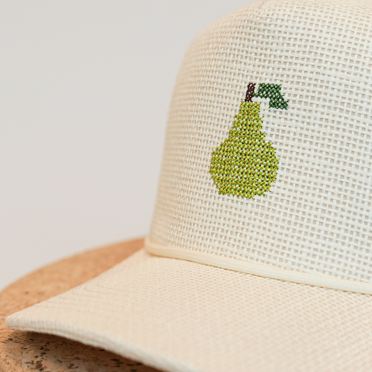Beige mesh cap with a green embroidered pear design on a light gray background