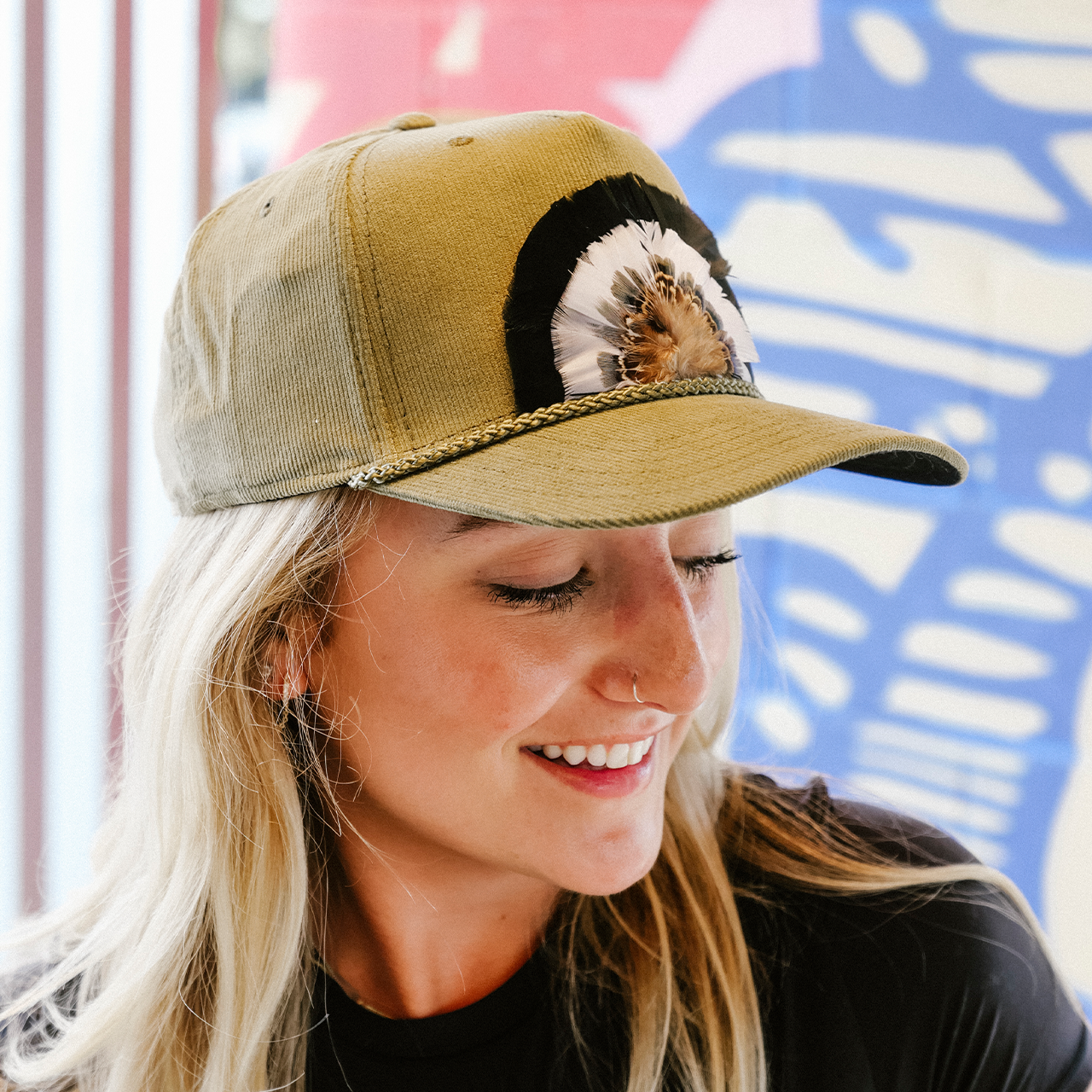 Woman wearing a tan baseball cap with a design, smiling against a colorful background
