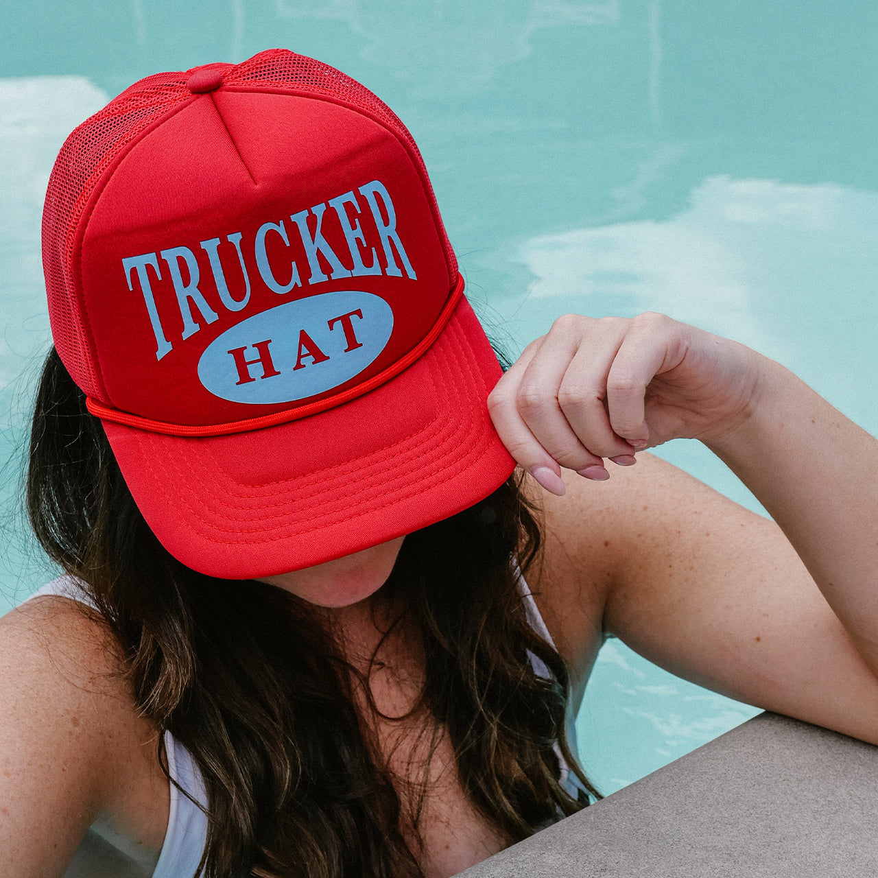 Red 'Trucker Hat' cap worn by a person with a pool in the background