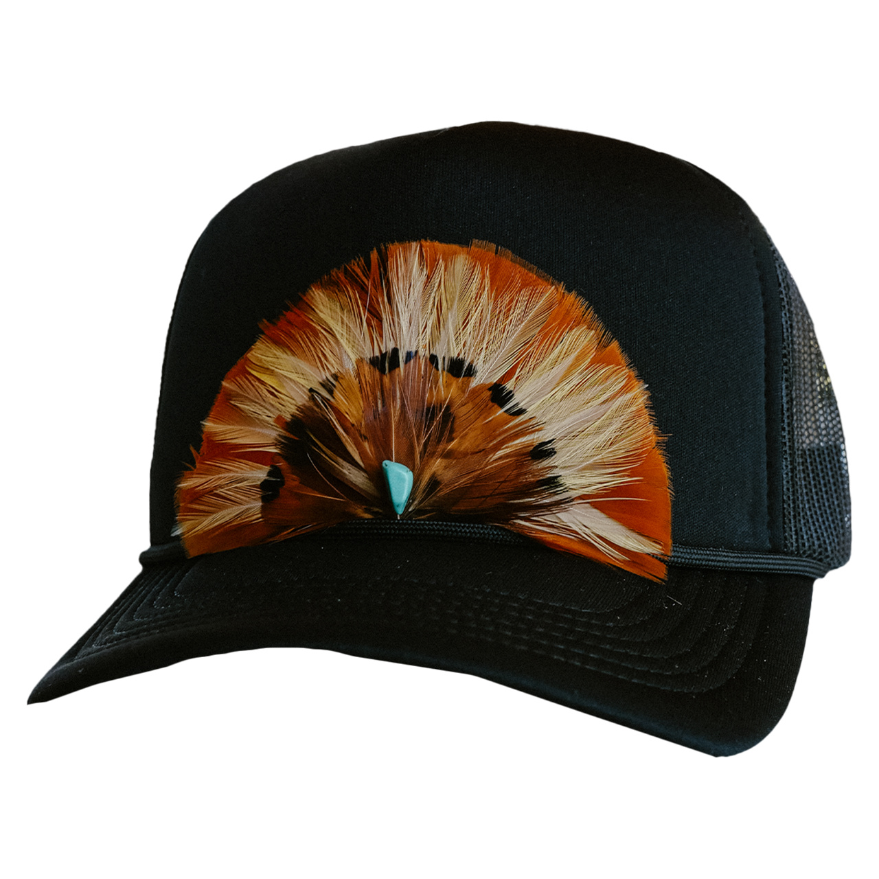 A black trucker hat with a hand-crafted feather detail on the front, displayed on a table with other hats in the background.