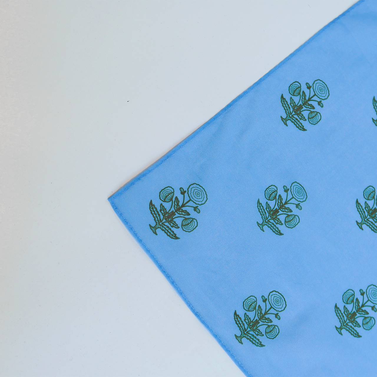 Blue fabric with green floral patterns on a light gray background