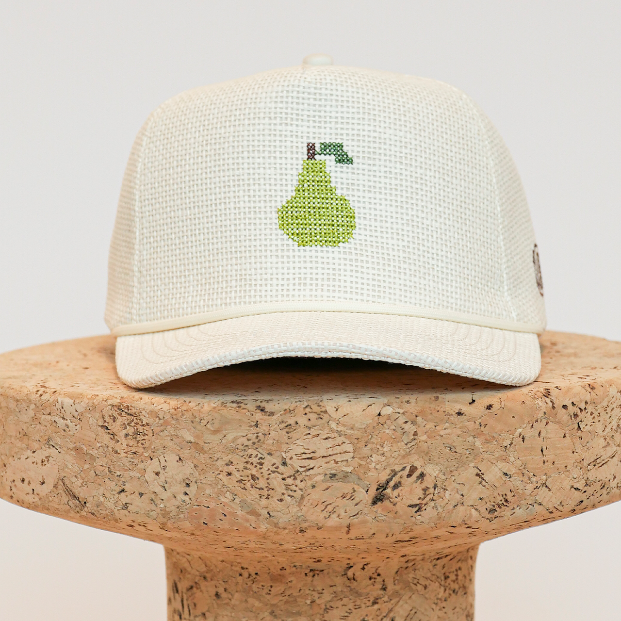 White cap with green embroidered design on a cork surface