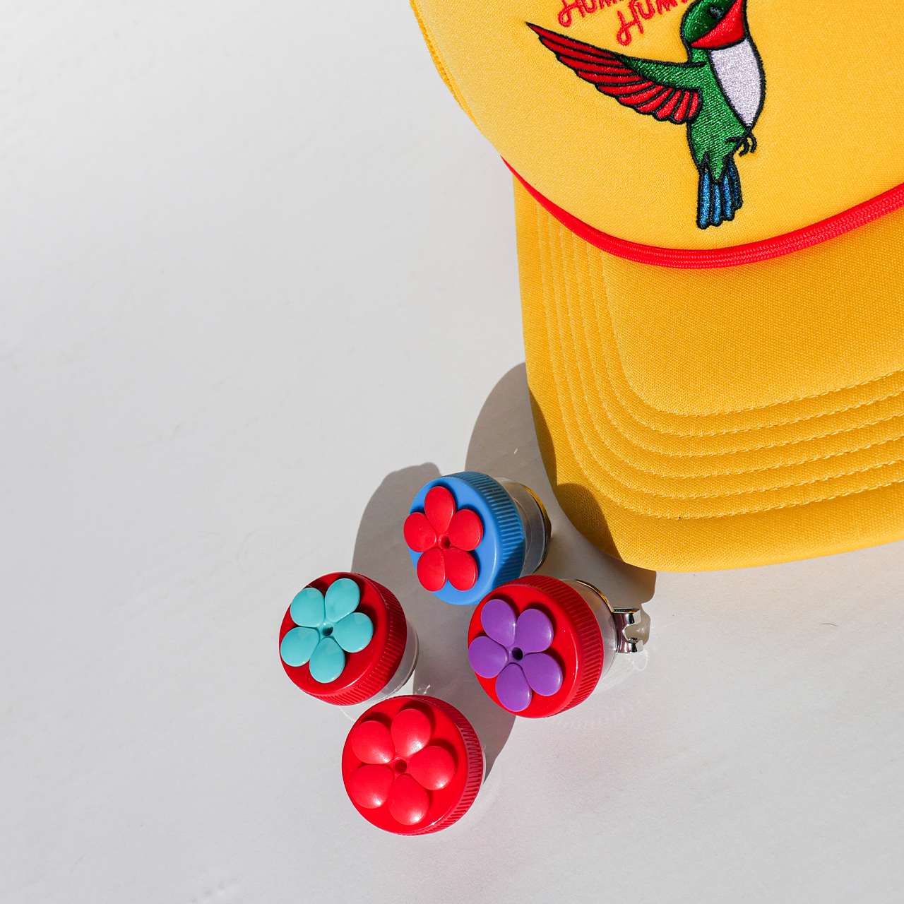 Yellow cap with bird design and colorful flower-shaped buttons on a light gray background