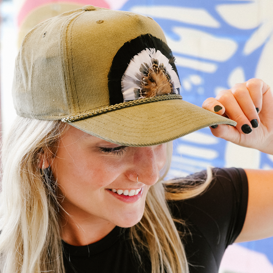 Woman wearing a tan cap with a decorative front panel, smiling outdoors.