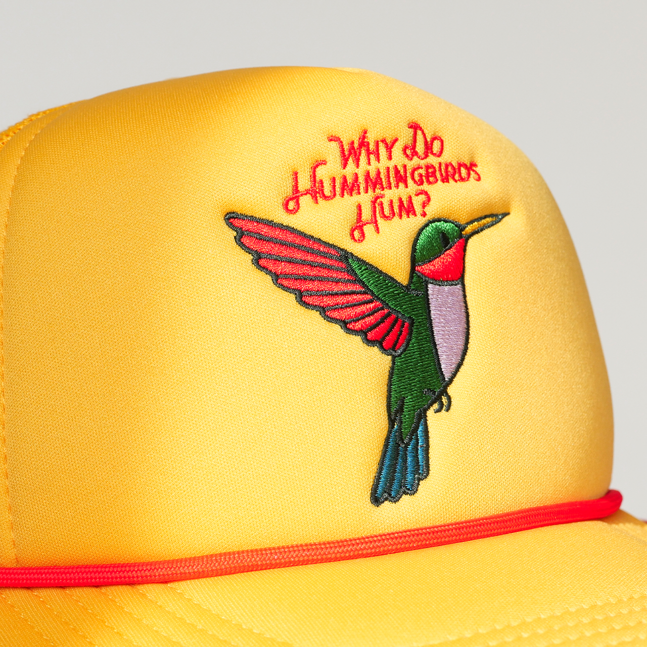 Yellow cap with embroidered hummingbird and text on a gray background
