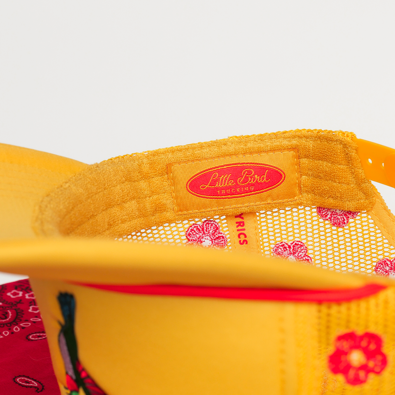 Yellow hat with floral patterns and 'Little Bird' branding on a white background