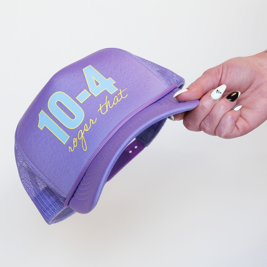 Purple cap with text held by a hand on a light gray background