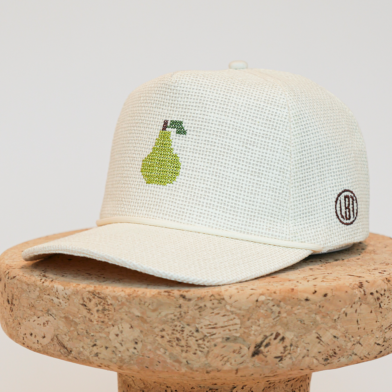White cap with green embroidered design on a cork block against a light gray background